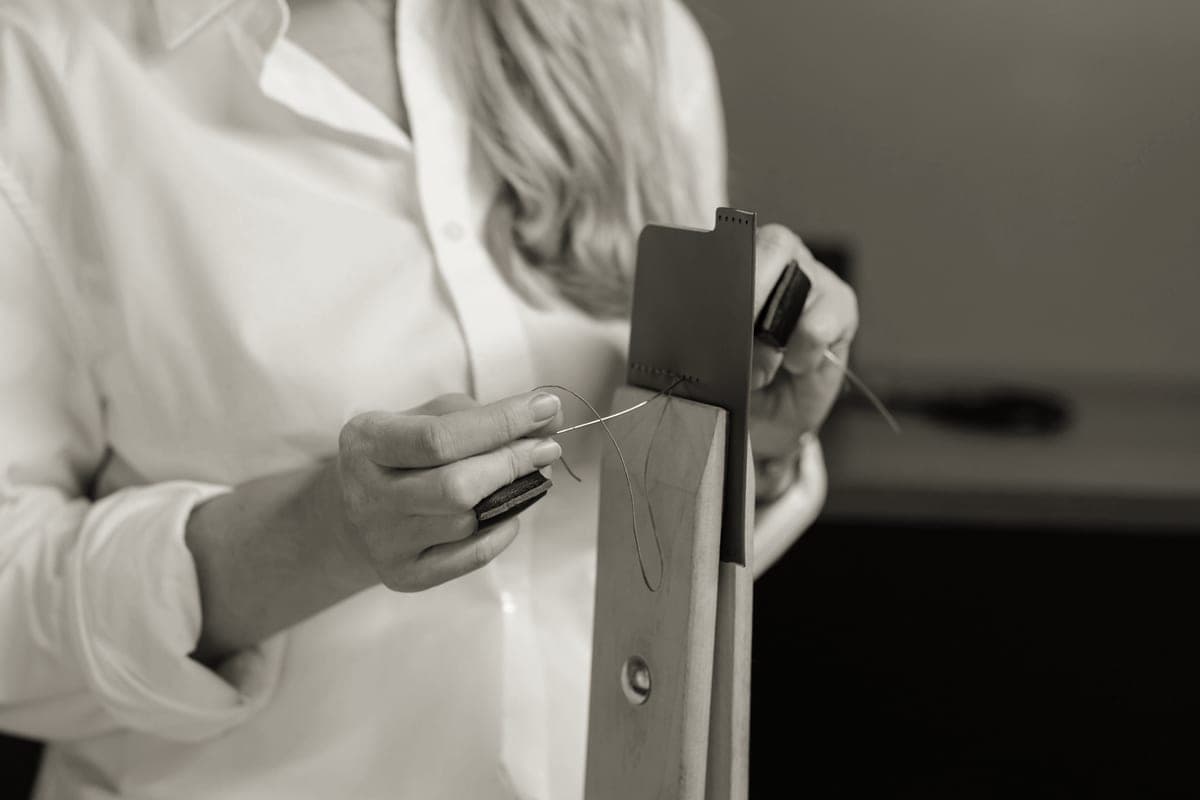 A craftsperson hand-stitching a piece of brown leather